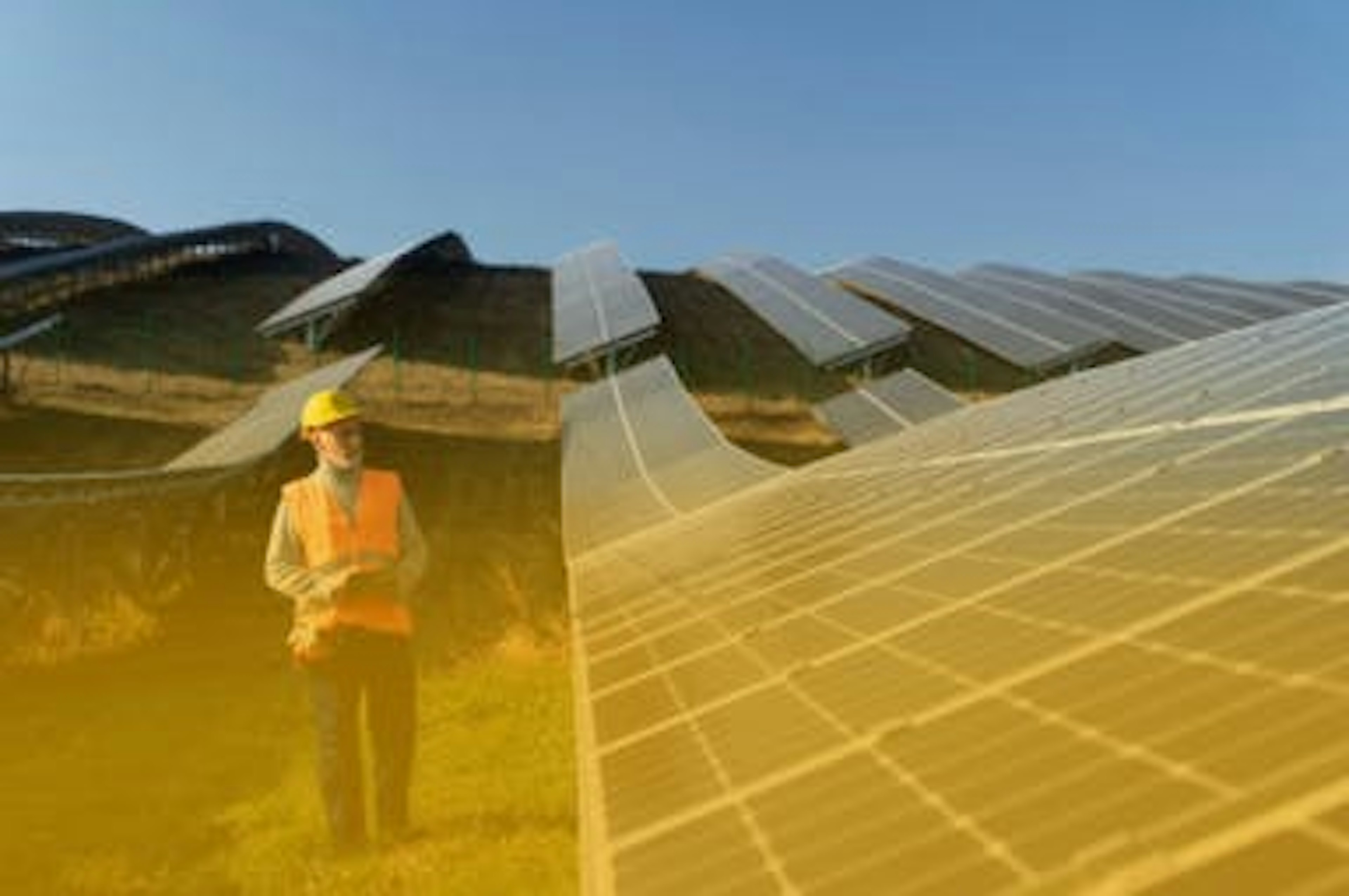 homem vestido com equipamentos de segurança em meio a um grande corredor de placas solares em cima de um campo verde