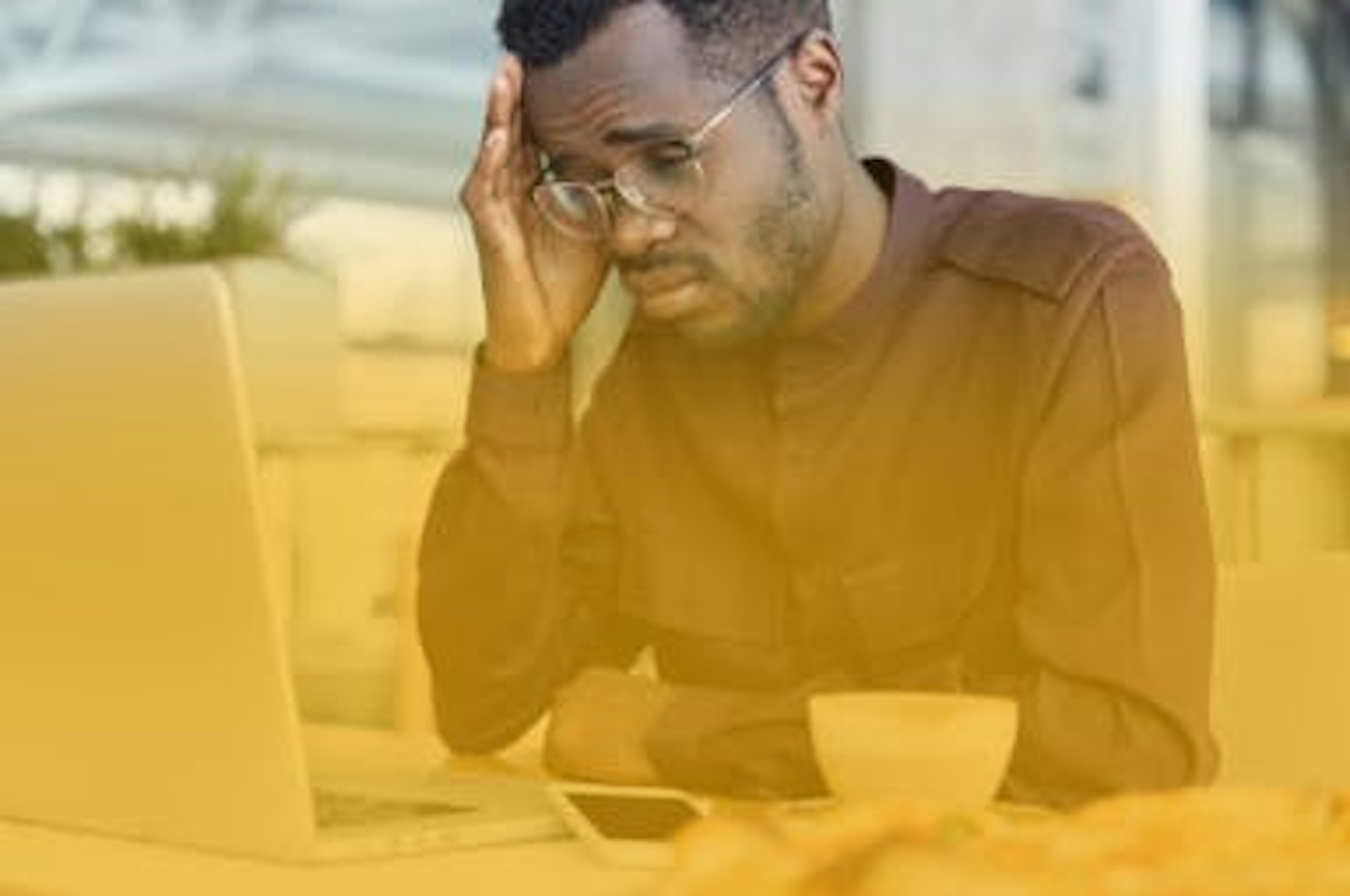 Homem negro, cansado e com expressão frustrada, olha desesperadamente para a tela do notebook ao consultar sua fatura de energia muito alta