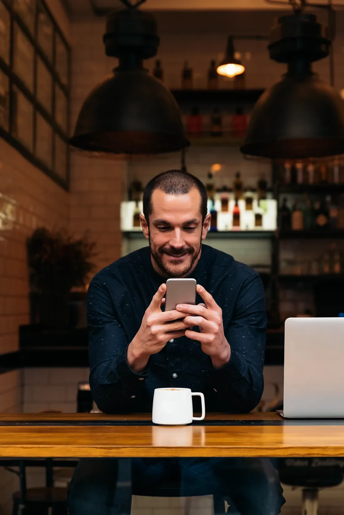 Man smiling while using his phone in a coffee shop